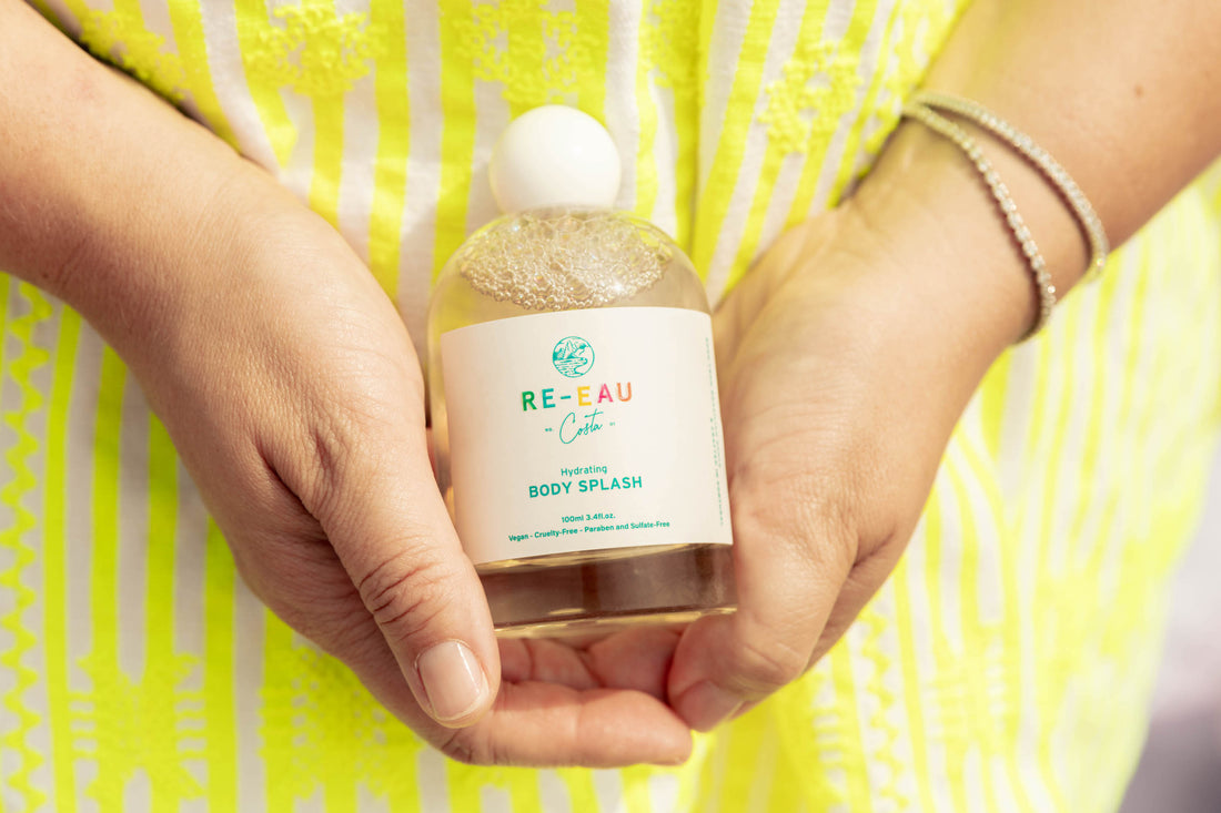 Photo of Re-Eau's creator Bell's hands holding a bottle of Re-Eau. She is wearing a striped yellow dress.